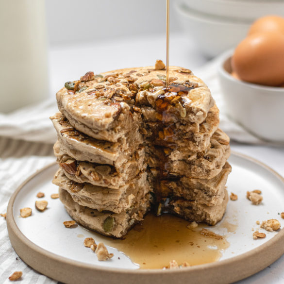 a stack of granola pancakes with syrup drizzling down the sides